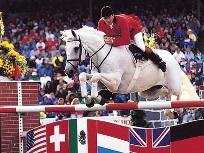 Equestrian rider and white horse clearing a red-and-white jump